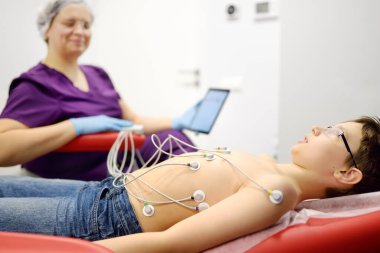 ECG testine tabi tutulan çocuk doktorla. Hasta çocuk vakum sensörleriyle tıp yatağında yatıyor. Pediyatrist tıbbi klinikte elektrokardiyogram işlemi sırasında tablet üzerinde sonuç arıyor. Kalbin kontrolü.