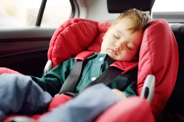Cute toddler boy sleeping in car seat. Portrait of pretty little child during family road trip. Safety transportation of baby by car. Long travel with children