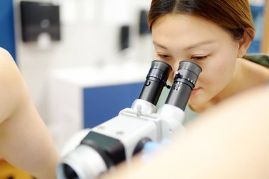 Jinekolog, jinekoloji koltuğunda mikroskop kullanan bir hastayı muayene ediyor. Doktor modern bir muayenehanede genç bir kıza koloskopi yapıyor. Rahim ağzı kanseri önleme ve teşhisi.