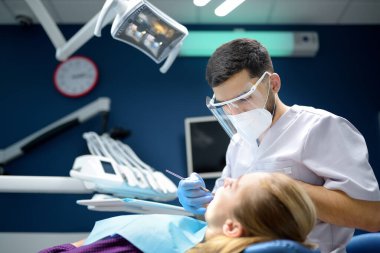Modern tıp merkezinde dişçi ve hasta. Doktor hastanede genç bir kadının dişlerini tedavi ediyor. Pratisyen, ortodontistlerden ya da protez tedavisinden önce hastayı muayene eder. Hijyen ve dişler sağlıklı.