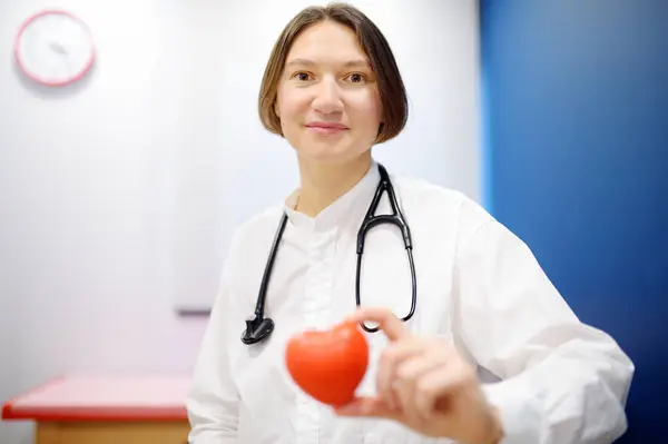 赤い心臓を持っている女性の心臓科医 赤い心臓は医師の手にかかっている カーディオロジーコンセプト ロイヤリティフリーのストック画像