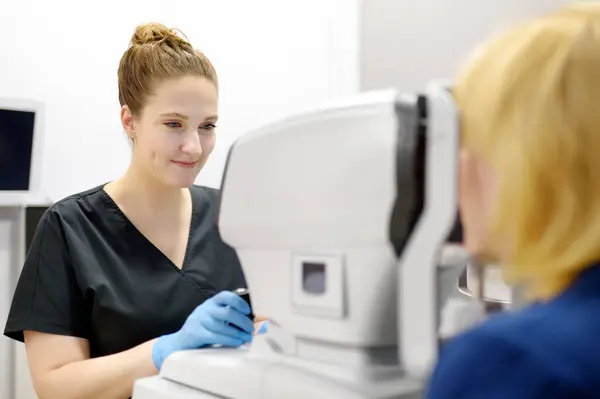 女性眼科医生用视网膜扫描仪检查成熟妇女的眼底 在视光师检查眼睑 晶状体 角膜的显微镜检查期间病人 — 图库照片