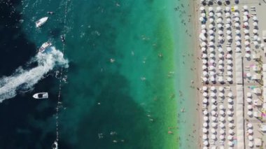 Sıcak bir yaz gününde insanlarla dolu bir plajın insansız hava görüntüsü. Tatil sezonu. Mükemmel kumlu bir sahilde beyaz güneş şemsiyeleri üst üste. En saf şeffaf Adriyatik Denizi