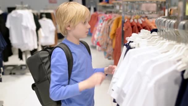 かわいい年齢の男の子は 店で自分自身のためにファッション服を選択します 子供と家族のためのショッピング 独立した子供がショッピングモールで母親を助ける 動画クリップ