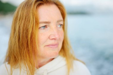 Deniz kıyısında yürüyen güzel yaşlı bayan. Mavi gözlü ve kızıl saçlı son sınıf öğrencisi bir kadının portresi..