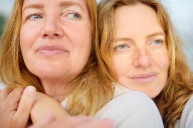 Kızıl saçlı kıdemli anne ve güzel yetişkin kızı birlikte yürüyüp gülüyorlar. Bir anne ve yetişkin çocuğunun mutlu bir buluşması. Sevimli bir kadın anneler gününde olgun annesine şefkatle sarılır.