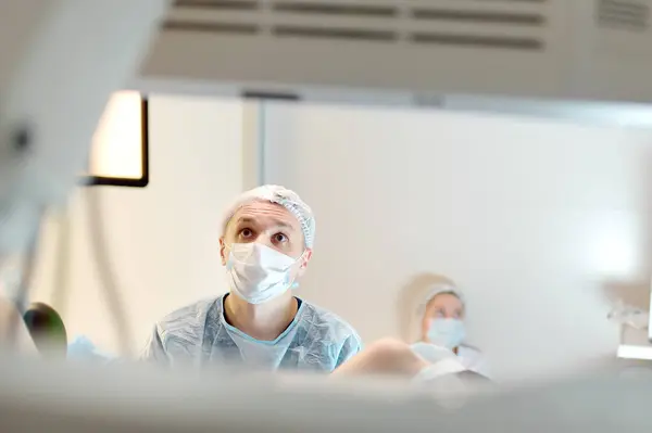 妇科医生在诊所的妇科椅子上给病人做手术 医生在现代医院实施侵入性医疗程序 在便携式屏幕上观察手术进展的外科医生 免版税图库照片