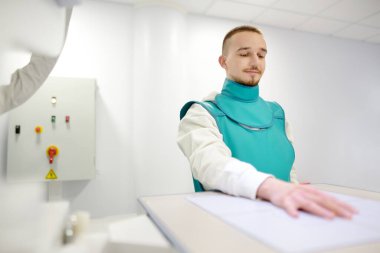 Modern klinikteki röntgen odasında kırık el röntgeni çektiren genç bir adam. Hasta kurşun önlük takıyor. İnsanların tıbbi muayenesi