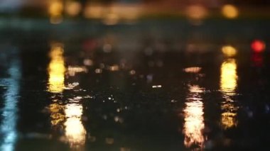 Bir gecede yağmur fırtınasının atmosferik videosu. Şiddetli yağmur ve alçak noktadan alınan su birikintilerinden geçen arabalardan sıçrama. Sokak lambalarının ışığında büyük damlalar kaldırıma düşer.