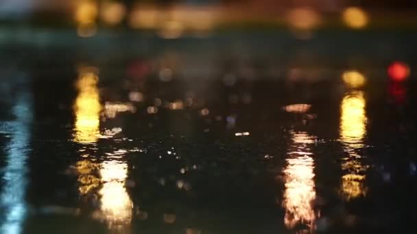 夜市での暴風雨の大気ビデオ 低点から撮影された水たまりを通過する車からの大雨とスプラッシュ 街灯の光の中で舗装上の大きな滴が壊れます スローモーション ロイヤリティフリーのストック動画