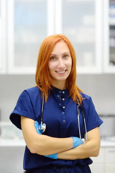 一位漂亮的红头发女医生在办公室预约病人时的垂直肖像是一个现代诊所 熟练的兽医在兽医医院工作 看着相机的女人 图库图片