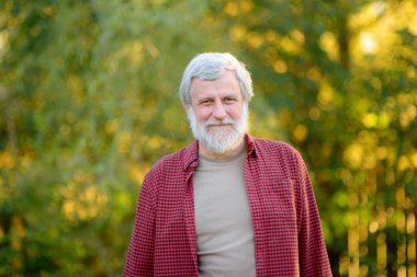 Güneşli bir yaz gününde, olgun yakışıklı bahçıvanın portresi. Gri saçlı yaşlı çiftçi kendi bahçesinde..