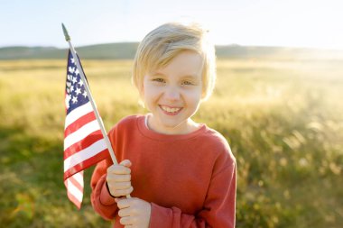 Cute little boy celebrating of July, 4 Independence Day of USA at sunny summer sunset. Child running with american flag of United States on wheat field. Proud little american boy holding country flag