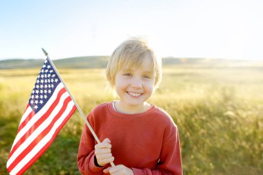 Cute little boy celebrating of July, 4 Independence Day of USA at sunny summer sunset. Child running with american flag of United States on wheat field. Proud little american boy holding country flag