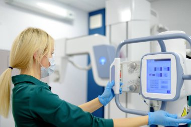 Kadın teknisyen röntgen cihazını ayarlıyor. Kadın radyolog modern kliniğin röntgen odasında bir hastanın röntgenini çekecek. İnsanların tıbbi muayenesi