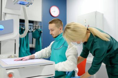 Modern klinikteki röntgen odasında genç bir adamın elinin röntgenini çekecek olan kadın radyolog. Hasta kurşun önlük takıyor. İnsanların tıbbi muayenesi