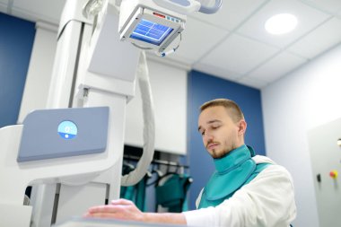 Modern klinikteki röntgen odasında kırık el röntgeni çektiren genç bir adam. Hasta kurşun önlük takıyor. İnsanların tıbbi muayenesi