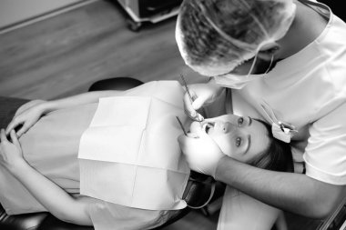 Modern tıp merkezinde dişçi ve hasta. Doktor hastanede genç bir kadının dişlerini tedavi ediyor. Pratisyen, ortodontistlerden ya da protez tedavisinden önce hastayı muayene eder. Siyah beyaz fotoğraf