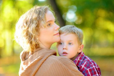 Sonbahar parkında yürürken bir anne ve oğlunun yakın plan portresi. Kadın, küçük oğlunu kollarına aldı ve ona nazikçe sarıldı. Küçük bir çocuk eğleniyor ve annesiyle takılıyor..