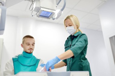 Modern klinikteki röntgen odasında kırık el röntgeni çektiren genç bir adam. Hasta kurşun önlük takıyor. İnsanların tıbbi muayenesi