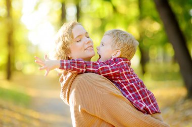 Sonbahar parkında yürürken bir anne ve oğlunun yakın plan portresi. Kadın, küçük oğlunu kollarına aldı ve ona nazikçe sarıldı. Küçük bir çocuk eğleniyor ve annesiyle takılıyor..