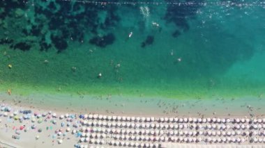 Sıcak bir yaz gününde insanlarla dolu bir plajın insansız hava görüntüsü. Tatil sezonu. Mükemmel kumlu bir sahilde beyaz güneş şemsiyeleri üst üste. En saf şeffaf Adriyatik Denizi