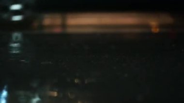 Bir gecede yağmur fırtınasının atmosferik videosu. Şiddetli yağmur ve alçak noktadan alınan su birikintilerinden geçen arabalardan sıçrama. Sokak lambalarının ışığında büyük damlalar kaldırıma düşer.