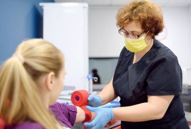 Bir flebotomist hemşire, bir damardan kan aldıktan sonra hastanın kolunu bandajlar. Genç bir kadın tıbbi muayene sırasında ya da bağış sürecinde laboratuvar testleri yapar.