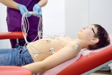 ECG testine tabi tutulan çocuk doktorla. Hasta çocuk vakum sensörleriyle tıp yatağında yatıyor. Bir hemşire bir kliniğin ofisinde kalp elektrokardiyogramı yapar. Kalbin kontrolü.