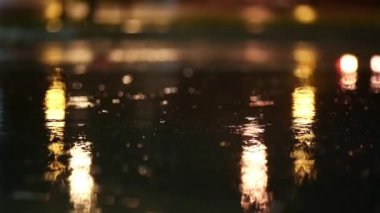 Bir gecede yağmur fırtınasının atmosferik videosu. Şiddetli yağmur ve alçak noktadan alınan su birikintilerinden geçen arabalardan sıçrama. Sokak lambalarının ışığında büyük damlalar kaldırıma düşer.