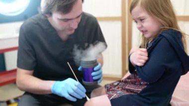 İlgili bir doktor küçük bir çocuğun derisindeki benleri ve siğilleri kontrol eder. Tatlı anaokulu kızı için sıvı nitrojenle iyi huylu tümörlerin alınması. Bebek tedavi korkusu.