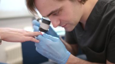 Romatologla randevusu olan bir hasta. Doktor, genç bir kadının tırnak yatağını ve kan damarlarını mikroskopla inceliyor. Romatolojik teşhisler. Dil altı melanom