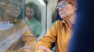 Güzel yaşlı bir kadın yerel bir tren vagonunda ya da dışarıda yağmur yağarken bir demiryolunda ata biniyor. Toplu taşıma sırasında yolcuların portresi. Yaşlı kadın yağmur penceresinden dışarı bakıyor.
