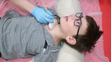Doktor, çocuk için ultrason yapıyor. Tarayıcı kullanıyor. Kadın doktor, tiroid bezi ve lenf düğümlerini taramak için hastanın boynuna ultrason sensörü takıyor. İç organların kontrolü