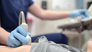 Doktor, tarayıcı kullanan bir çocuk için karın ultrasonu yapıyor. Kadın doktor, ultrason sensörünü hastanın karnına yerleştirip ekrana bakıyor. Okul çocukları için iç organların tıbbi muayenesi