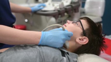 Doktor, çocuk için ultrason yapıyor. Tarayıcı kullanıyor. Kadın doktor, tiroid bezi ve lenf düğümlerini taramak için hastanın boynuna ultrason sensörü takıyor. İç organların kontrolü