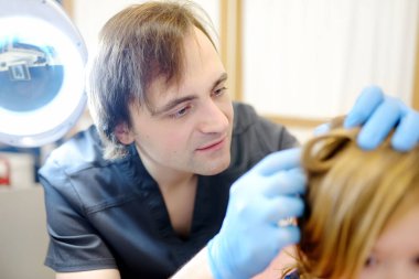 Portrait of cute little girl during appointment of dermatologist in modern clinic. Doctor examines child hair and scalp for lice and nits. Pediculosis and parasitic diseases are common in kids groups clipart