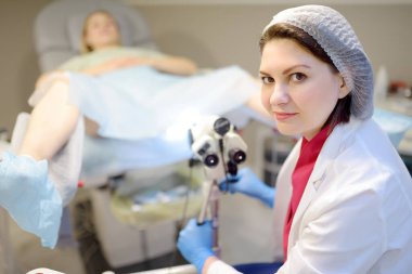 Jinekolog, jinekoloji koltuğunda mikroskop kullanan bir hastayı muayene ediyor. Doktor modern bir muayenehanede genç bir kıza koloskopi yapıyor. Rahim ağzı kanseri önleme ve teşhisi.