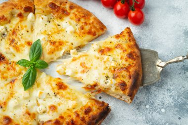 Italian pizza four cheeses with stretching cheese and basil on a light concrete background.