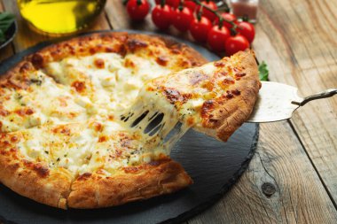 A slice of hot Italian pizza with stretching cheese. Pizza four cheeses with basil on a wooden background.
