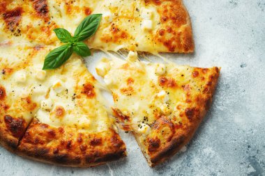 Italian pizza four cheeses with stretching cheese and basil on a light concrete background.