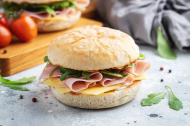 İki ev yapımı sandviç, jambon, peynir ve roka ile beton bir masada. Hafif arka planda iki hamburger..