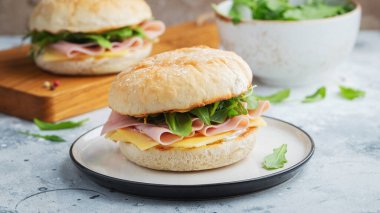İki ev yapımı sandviç, jambon, peynir ve roka ile beton bir masada. Hafif arka planda iki hamburger..