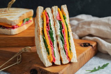 Two homemade sandwiches with sausage, cheese and arugula on a light concrete background. The concept of a quick meal or snack at work or school. With copy space