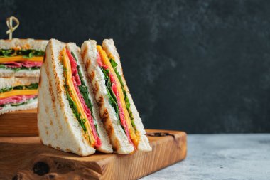 Two homemade sandwiches with sausage, cheese and arugula on a light concrete background. The concept of a quick meal or snack at work or school. With copy space