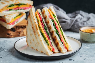 Two homemade sandwiches with sausage, cheese and arugula on a light concrete background. The concept of a quick meal or snack at work or school. With copy space