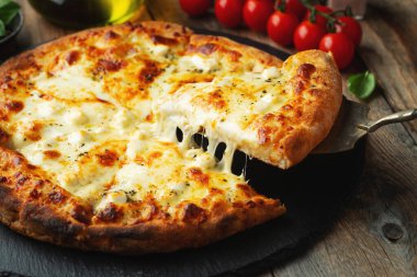 A slice of hot Italian pizza with stretching cheese. Pizza four cheeses with basil on a wooden background.