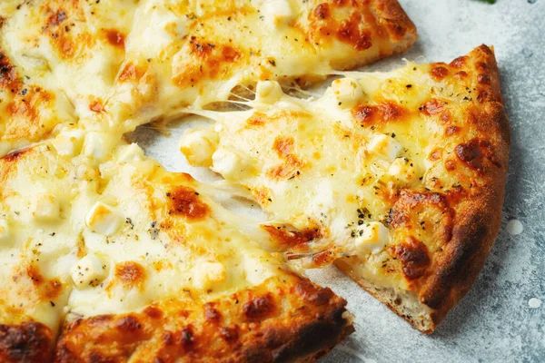 Italian pizza four cheeses with stretching cheese and basil on a light concrete background.