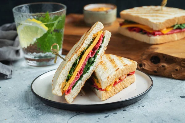 Two homemade sandwiches with sausage, cheese and arugula on a light concrete background. The concept of a quick meal or snack at work or school.