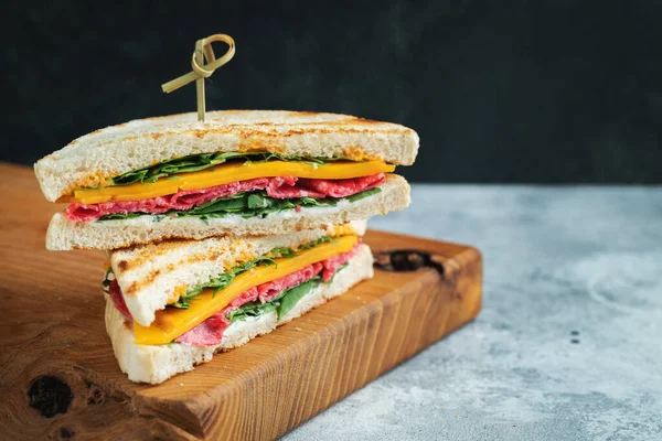 Two homemade sandwiches with sausage, cheese and arugula on a light concrete background. The concept of a quick meal or snack at work or school. With copy space